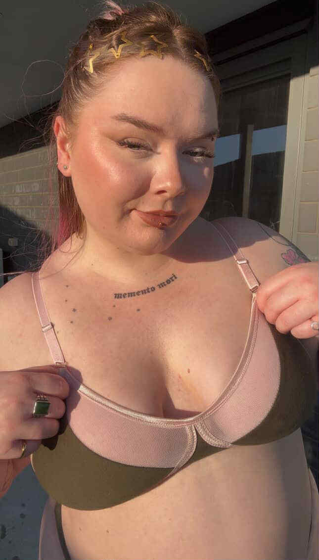Person standing outdoors in pink and olive bra from Valerie Lingerie, styled with gold star hair clips and visible chest tattoos.