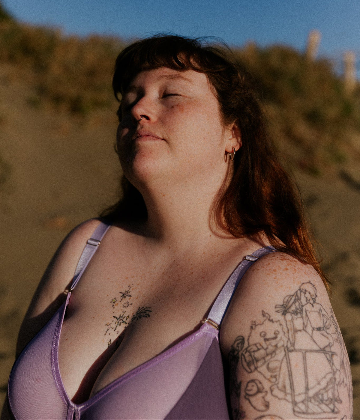 Woman with tattoos wearing a lavender bra on a beach