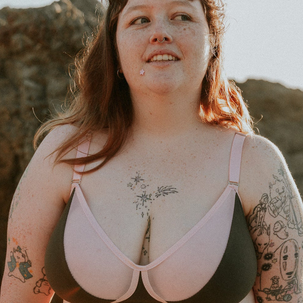 Person wearing a green and pink bralette with tattoos on arms and chest, standing outdoors.