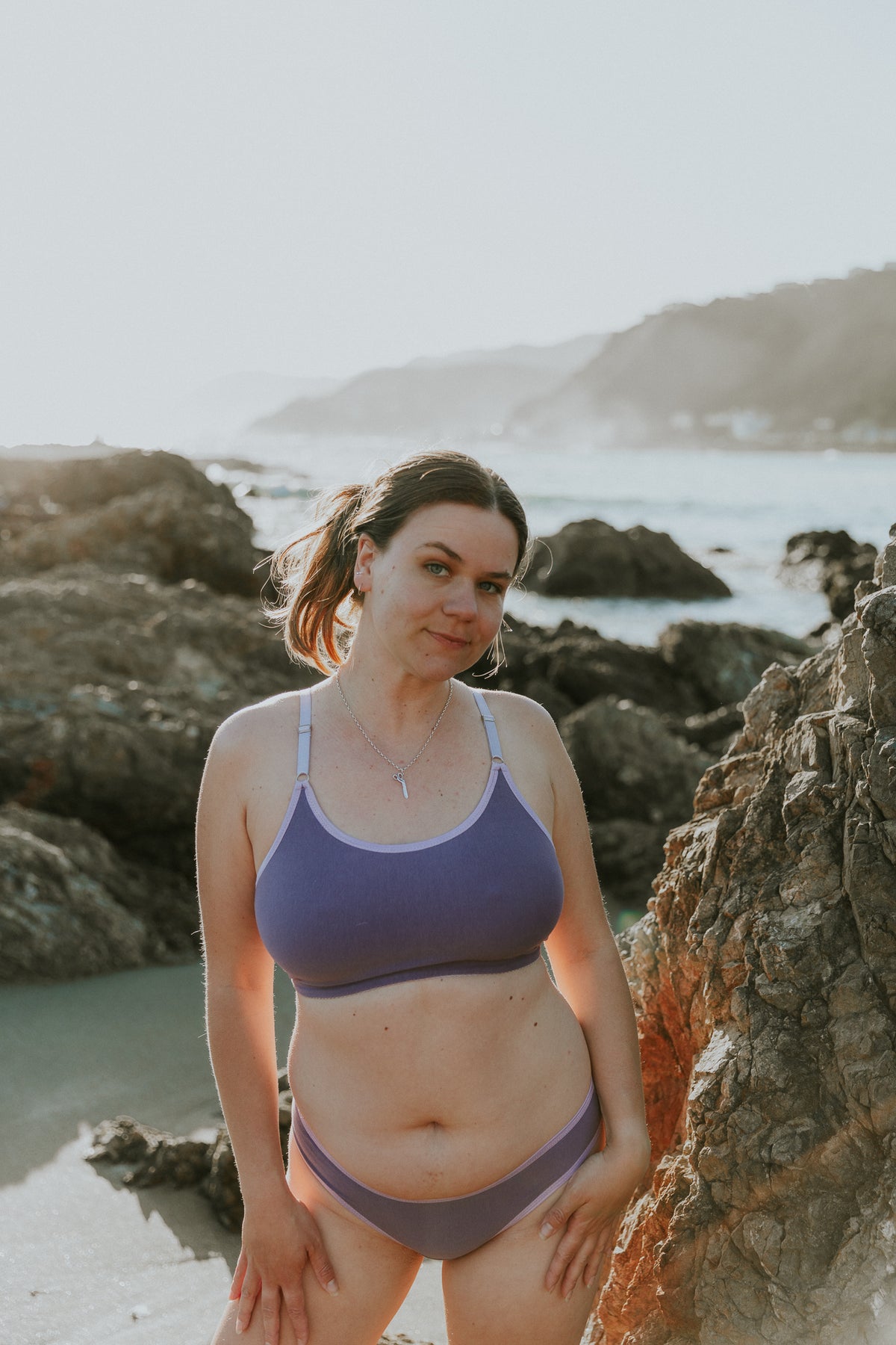 Lynne crop bra in lilac organic cotton with matching briefs, worn on a rocky beach, from Valerie Lingerie